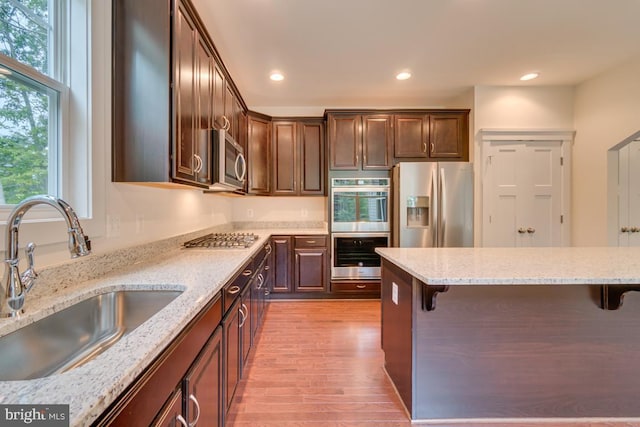 kitchen with light stone countertops, appliances with stainless steel finishes, sink, and a breakfast bar area