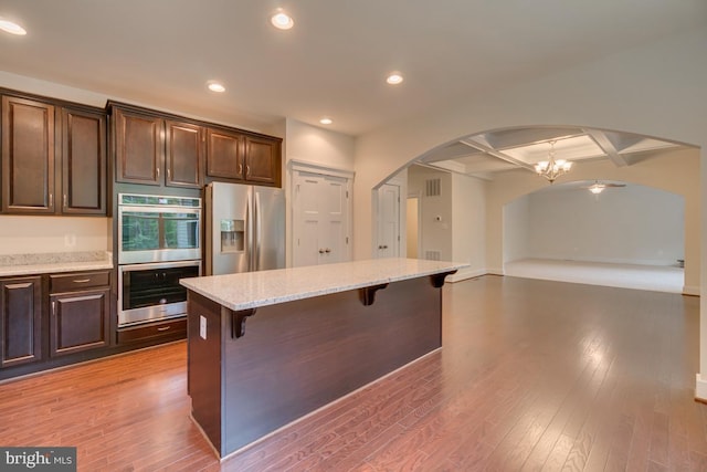 kitchen with appliances with stainless steel finishes, beamed ceiling, an inviting chandelier, a breakfast bar area, and coffered ceiling