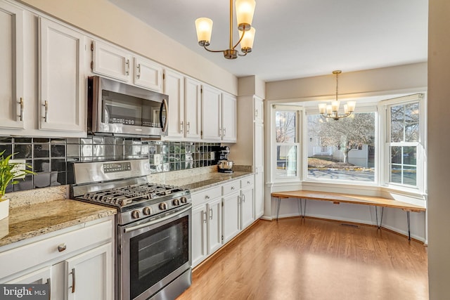 kitchen featuring white cabinetry, decorative light fixtures, a chandelier, appliances with stainless steel finishes, and backsplash