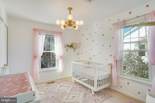 carpeted bedroom featuring a crib and a chandelier