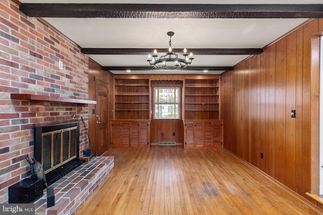 unfurnished living room with beam ceiling, built in features, wood walls, and a chandelier