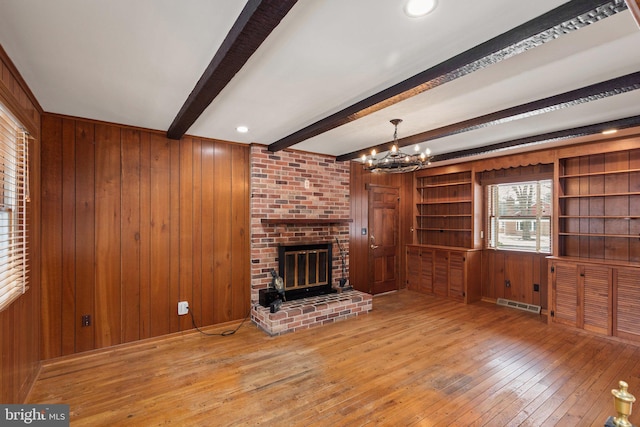 unfurnished living room with a notable chandelier, wood walls, beamed ceiling, and a fireplace