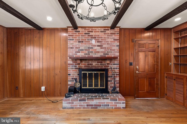 living room with wood walls, light hardwood / wood-style flooring, beam ceiling, and a fireplace