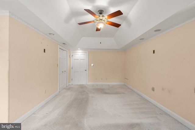 empty room with ceiling fan, a tray ceiling, and light carpet