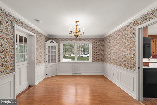 unfurnished dining area with light hardwood / wood-style flooring, ornamental molding, and a notable chandelier