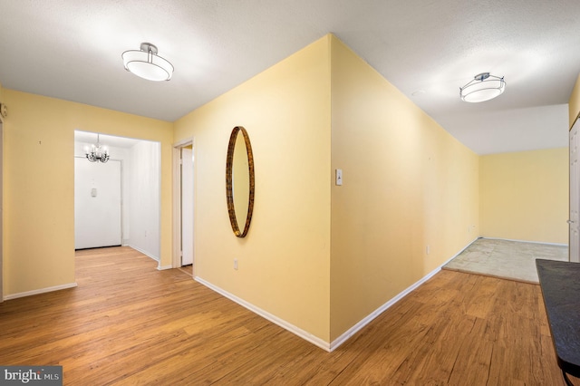 hallway with an inviting chandelier, a textured ceiling, and light hardwood / wood-style flooring