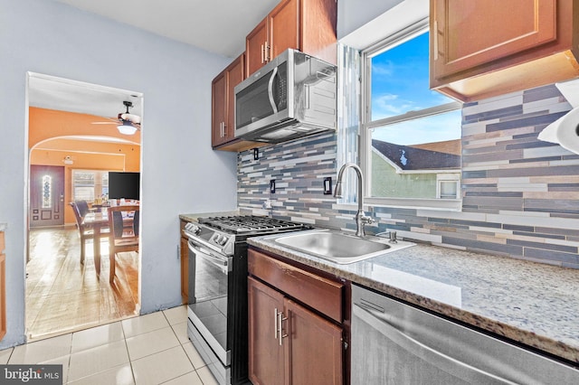 kitchen with stainless steel appliances, sink, light stone counters, light tile patterned flooring, and backsplash