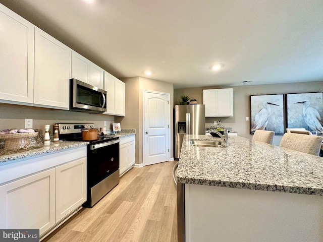 kitchen featuring stainless steel appliances, sink, white cabinets, light wood-type flooring, and a kitchen island with sink