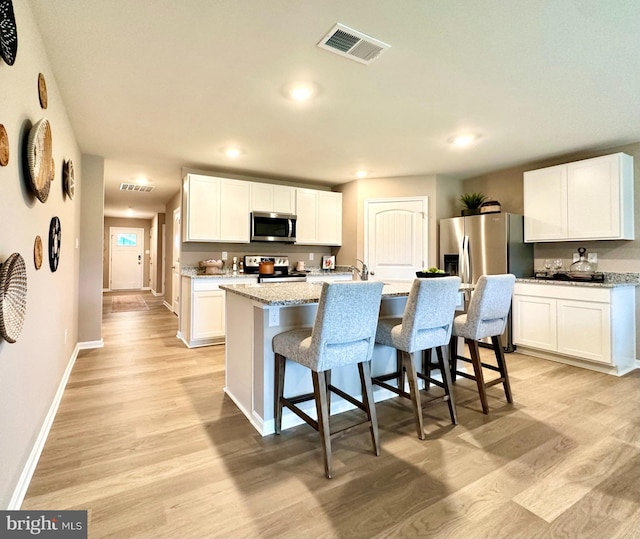 kitchen featuring stainless steel appliances, a center island with sink, white cabinetry, and light stone counters