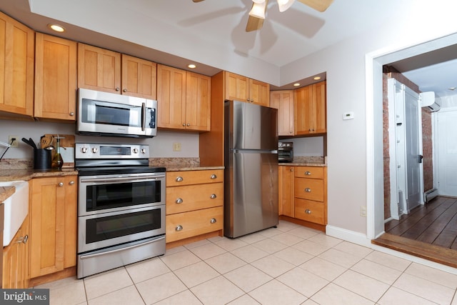 kitchen with a wall unit AC, ceiling fan, stainless steel appliances, baseboard heating, and light stone countertops