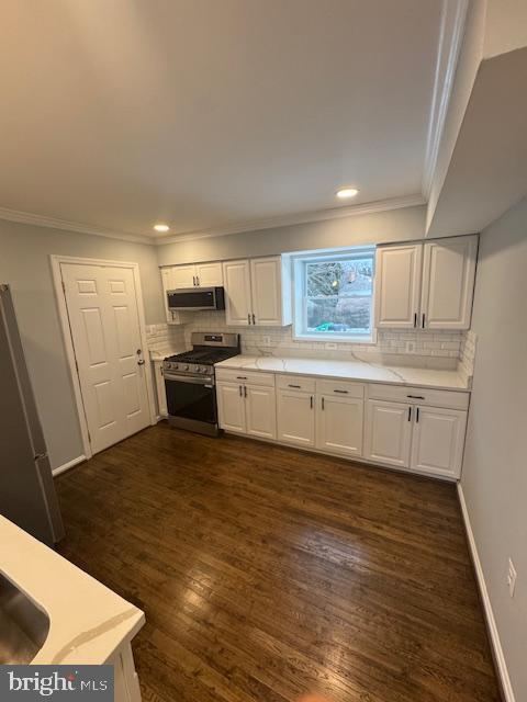 kitchen with dark hardwood / wood-style flooring, appliances with stainless steel finishes, backsplash, and white cabinets