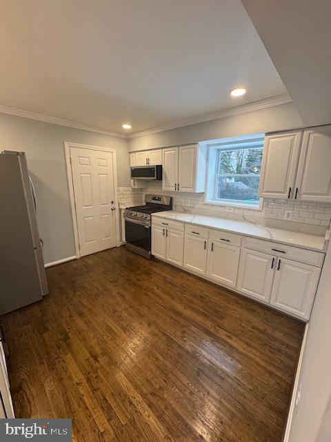 kitchen featuring white cabinets, appliances with stainless steel finishes, dark wood-type flooring, decorative backsplash, and crown molding