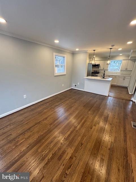 unfurnished living room featuring sink, dark hardwood / wood-style floors, a wealth of natural light, and crown molding