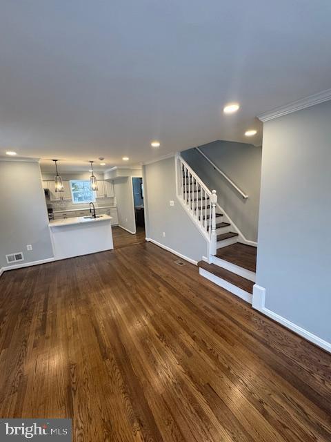 unfurnished living room featuring a notable chandelier, crown molding, dark hardwood / wood-style floors, and sink