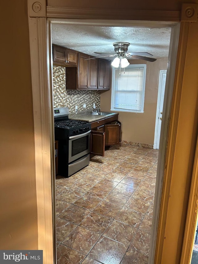 kitchen with a textured ceiling, ceiling fan, tasteful backsplash, stainless steel gas range oven, and dark brown cabinets