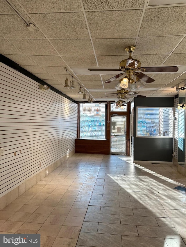 unfurnished sunroom featuring rail lighting, ceiling fan, and a paneled ceiling