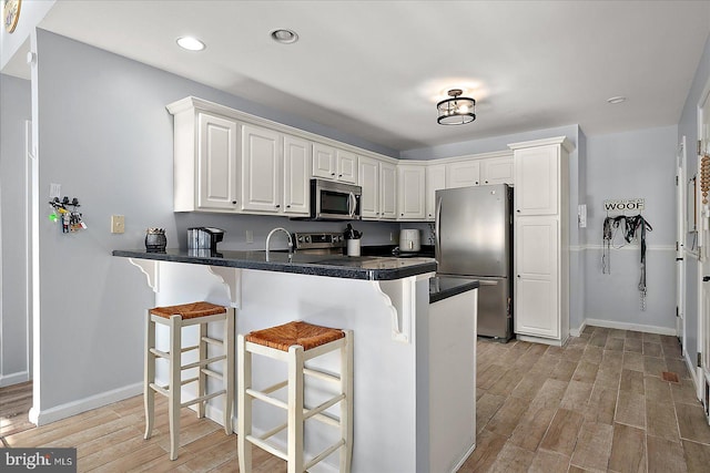 kitchen with white cabinets, stainless steel appliances, kitchen peninsula, light hardwood / wood-style flooring, and a breakfast bar area