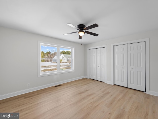 unfurnished bedroom featuring two closets, light hardwood / wood-style flooring, and ceiling fan