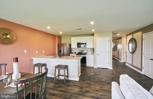 kitchen with dark wood-type flooring, a kitchen island with sink, white cabinets, appliances with stainless steel finishes, and a kitchen breakfast bar