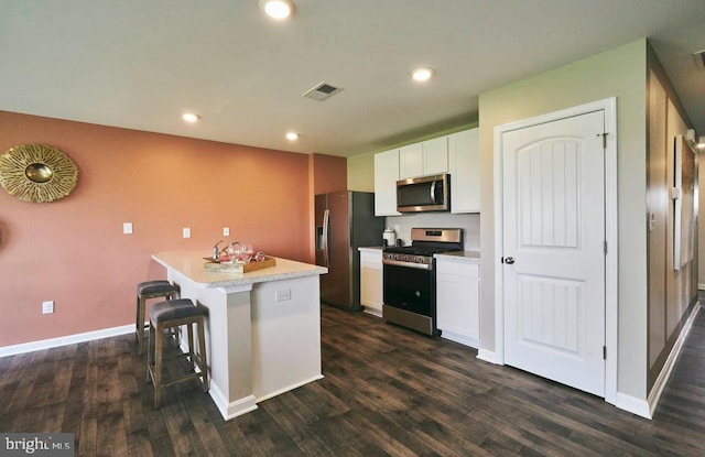 kitchen with stainless steel appliances, white cabinets, a breakfast bar, and dark hardwood / wood-style floors