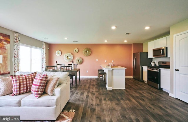 kitchen with stainless steel appliances, white cabinetry, a breakfast bar area, dark hardwood / wood-style floors, and a kitchen island with sink