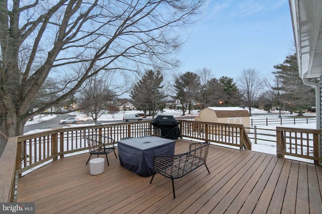 snow covered deck featuring a shed and area for grilling