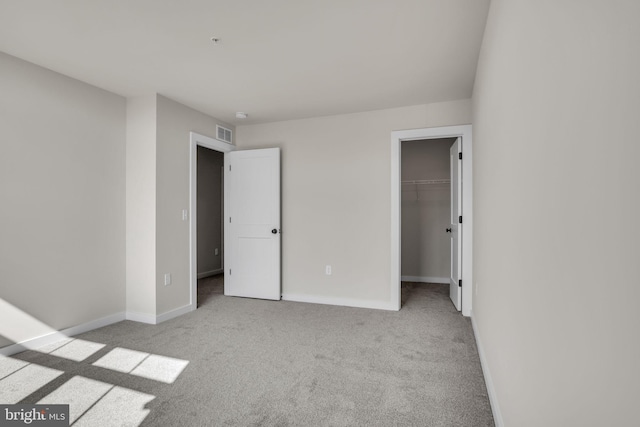 unfurnished bedroom featuring carpet floors, a walk in closet, visible vents, and baseboards