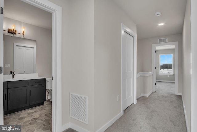 hallway featuring light colored carpet, visible vents, and baseboards