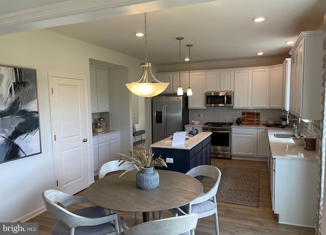 kitchen featuring white cabinetry, backsplash, hanging light fixtures, a kitchen island, and appliances with stainless steel finishes