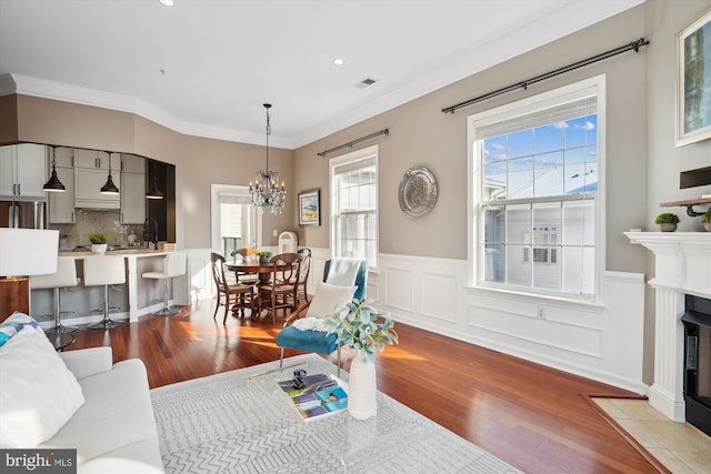 living room with ornamental molding, a chandelier, a wealth of natural light, and light hardwood / wood-style floors