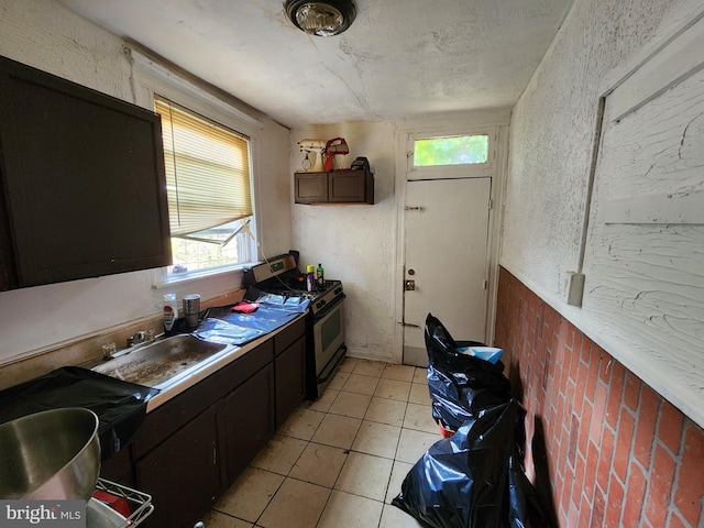 kitchen with sink, dark brown cabinets, light tile patterned flooring, and stainless steel stove