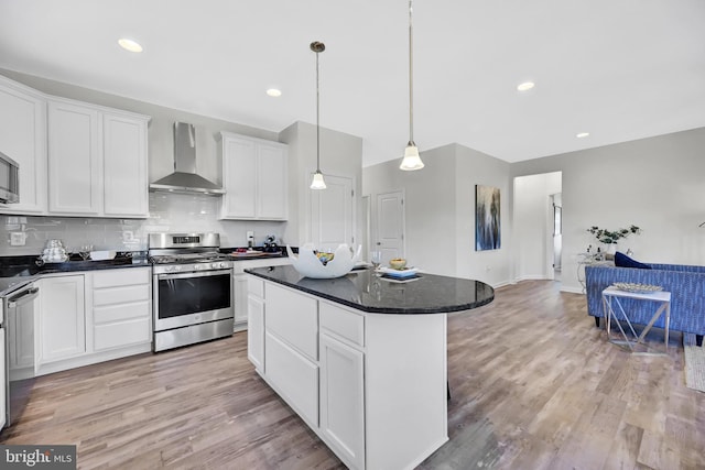 kitchen with decorative light fixtures, a center island, white cabinetry, wall chimney range hood, and gas range