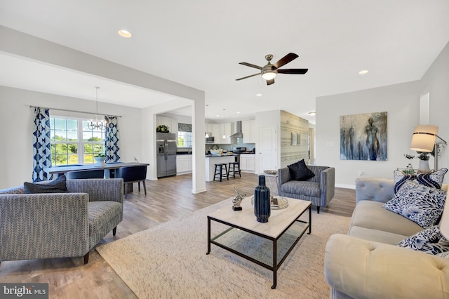 living room with light wood-type flooring and ceiling fan with notable chandelier