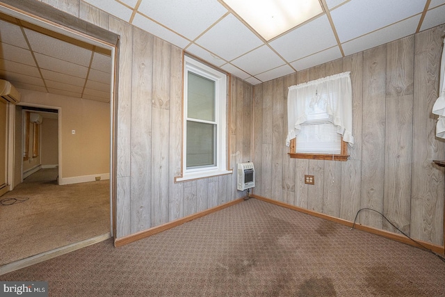 carpeted spare room with wood walls, a wall mounted AC, a drop ceiling, and heating unit