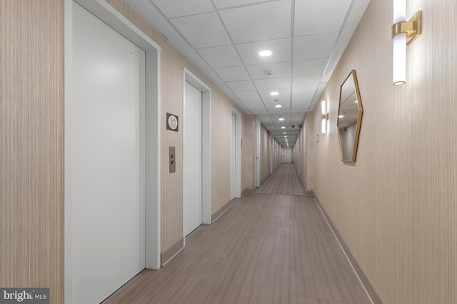 hallway featuring light hardwood / wood-style floors, a drop ceiling, and elevator