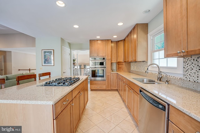 kitchen with stainless steel appliances, light stone counters, a kitchen island, and sink