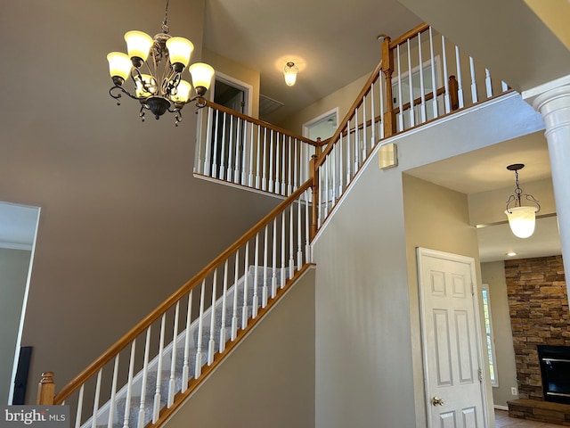 stairway with a towering ceiling, a stone fireplace, and a notable chandelier