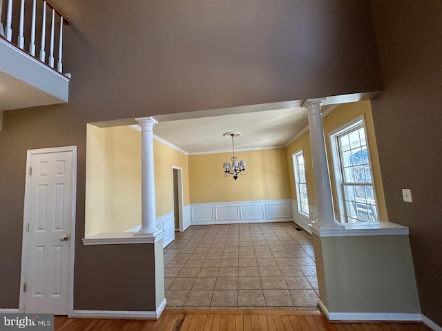 unfurnished dining area featuring an inviting chandelier, ornamental molding, decorative columns, and light wood-type flooring