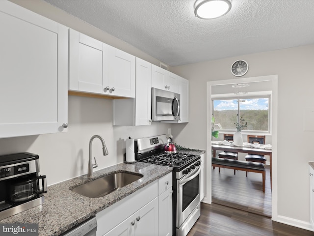 kitchen featuring appliances with stainless steel finishes, white cabinets, dark wood-type flooring, and a sink