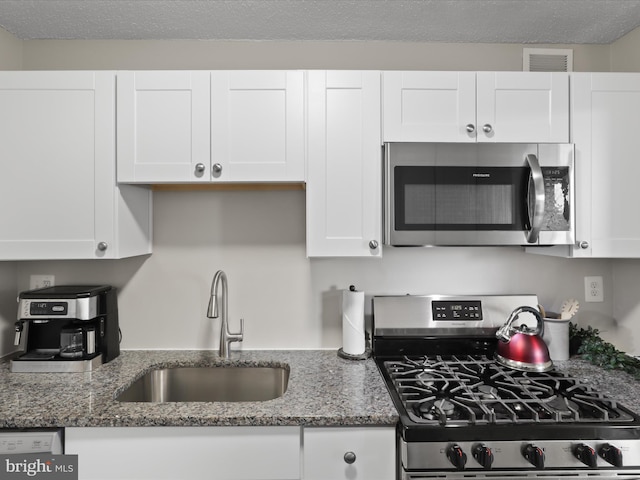 kitchen with stainless steel appliances, white cabinets, a sink, and visible vents