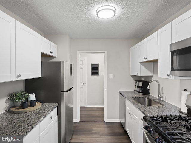 kitchen with stainless steel appliances, dark stone countertops, a sink, and white cabinets