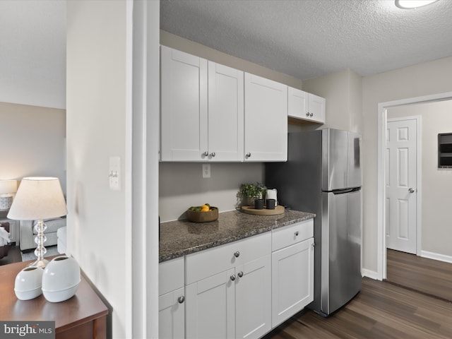 kitchen featuring a textured ceiling, dark wood-type flooring, white cabinets, freestanding refrigerator, and dark stone countertops