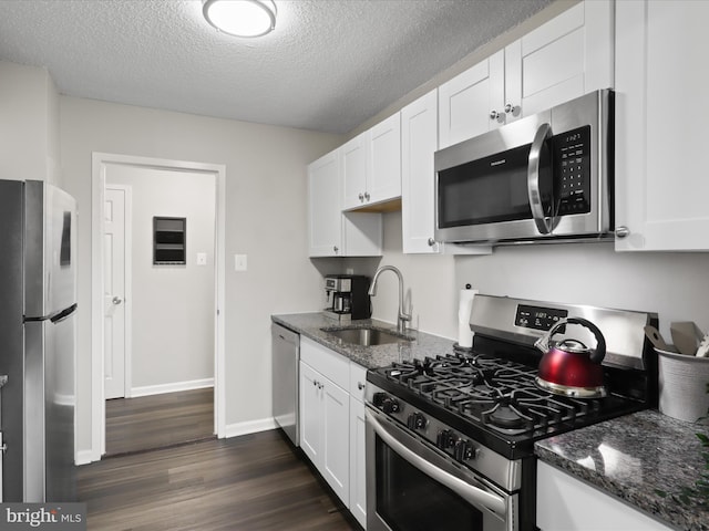 kitchen featuring white cabinets, dark stone counters, stainless steel appliances, and a sink