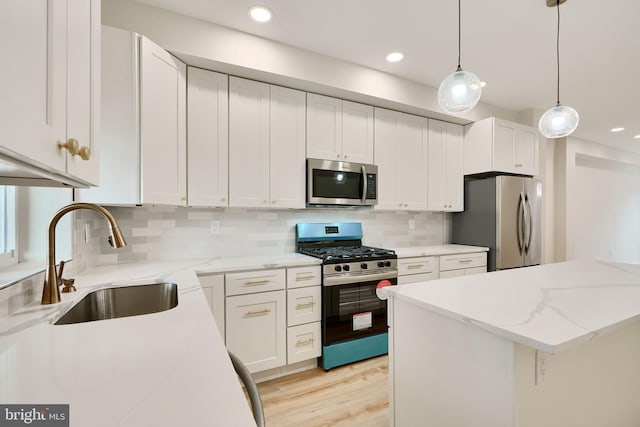 kitchen featuring a sink, white cabinets, hanging light fixtures, appliances with stainless steel finishes, and light stone countertops