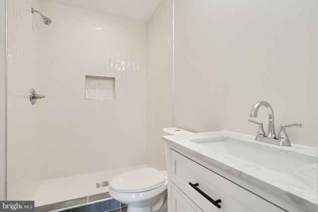 bathroom with toilet, tiled shower, and vanity