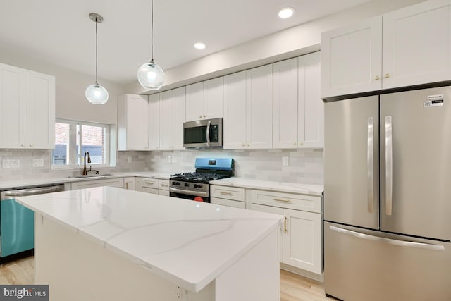 kitchen featuring light stone counters, stainless steel appliances, white cabinetry, a sink, and a kitchen island