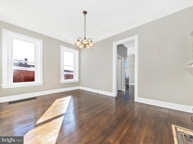 unfurnished dining area featuring dark wood-type flooring, a textured ceiling, and a notable chandelier