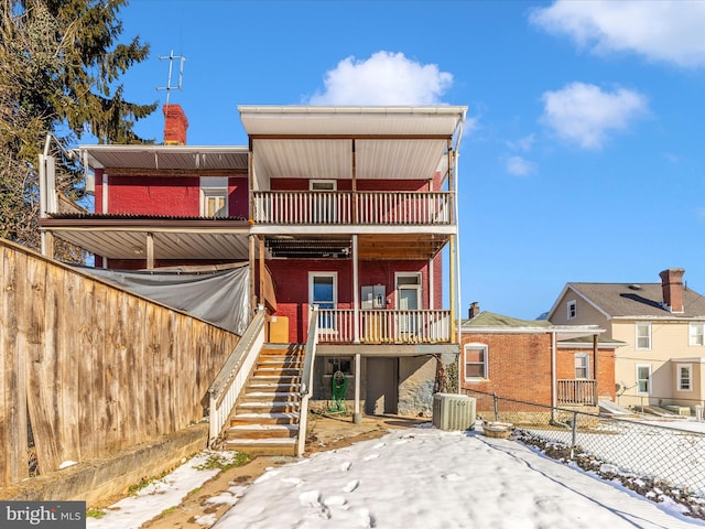 snow covered back of property with cooling unit and a balcony