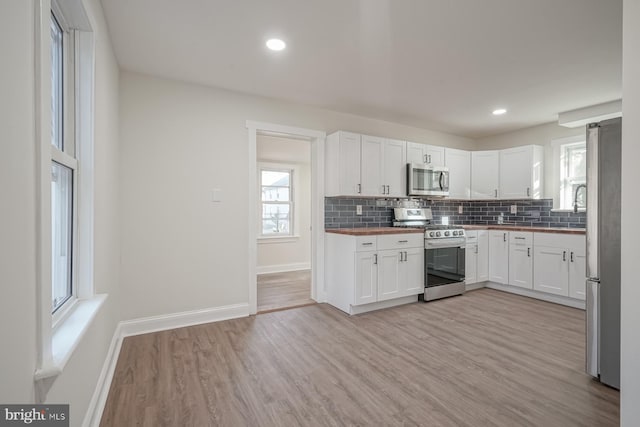 kitchen featuring wooden counters, stainless steel appliances, light wood-type flooring, white cabinetry, and tasteful backsplash