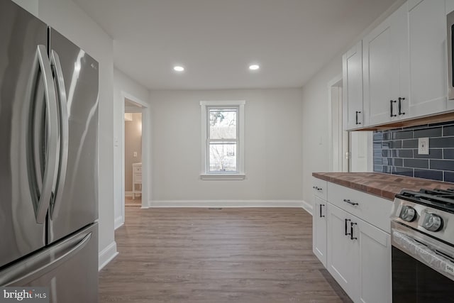 kitchen featuring white cabinets, appliances with stainless steel finishes, butcher block countertops, and decorative backsplash